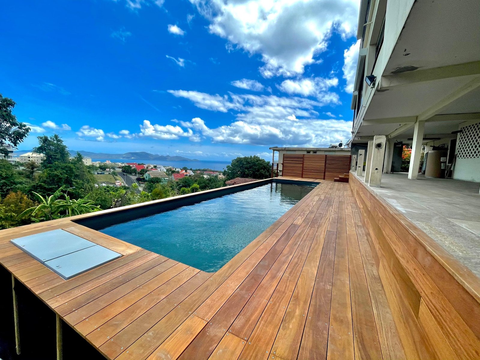 Deck en bois entourant une piscine avec vue sur la Martinique